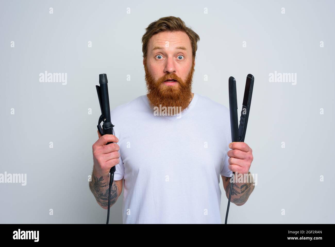 Wunderter Mann mit Haarglätter ist bereit zu arbeiten Stockfoto