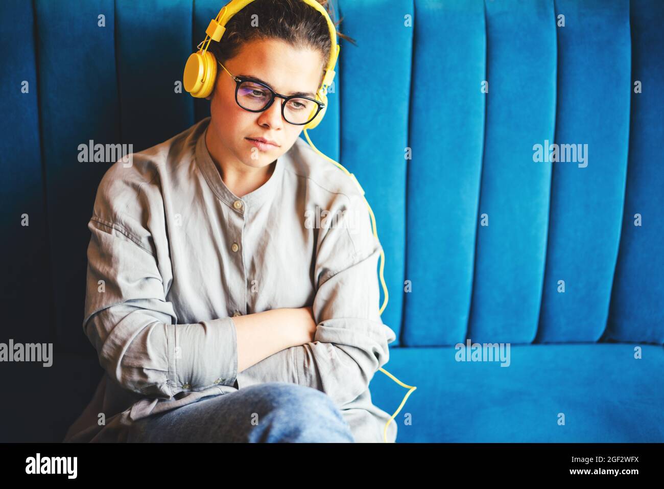 Traurige junge Frau, die mit Kopfhörern Musik hört. Sie wirkt einsam, deprimiert, müde, hat negative Emotionen. Psychische Gesundheit und Stressmanagement Thema Stockfoto