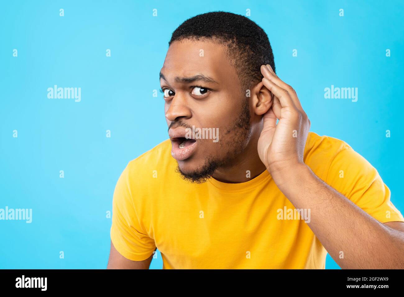 Afroamerikanischer Guy Listening Hand Am Ohr Halten, Blauer Hintergrund Stockfoto