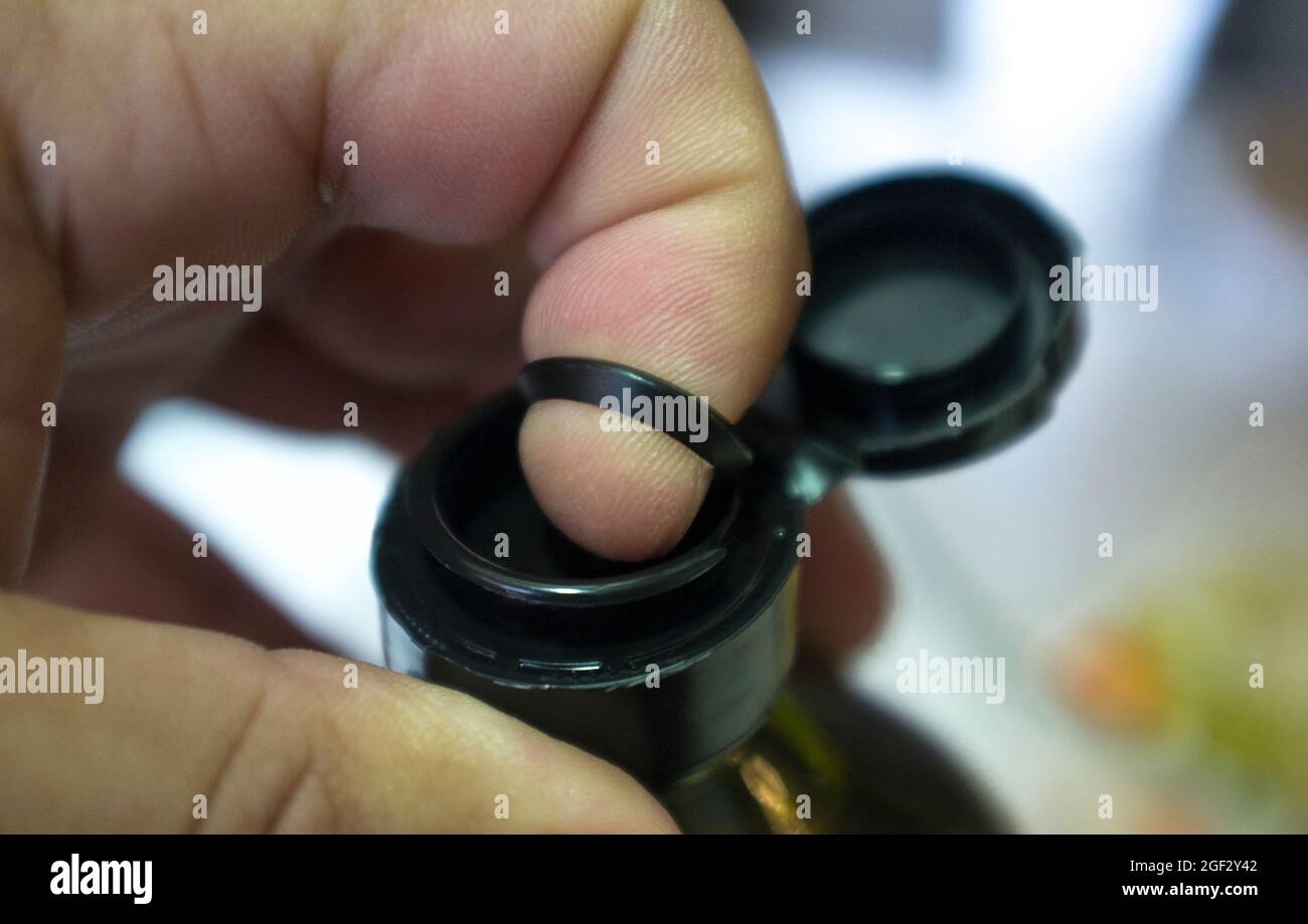 Öffnen einer versiegelten Olivenölflasche mit Finger und einer inneren herausziehbaren Kunststofflasche unter der Kappe. Nahaufnahme Stockfoto