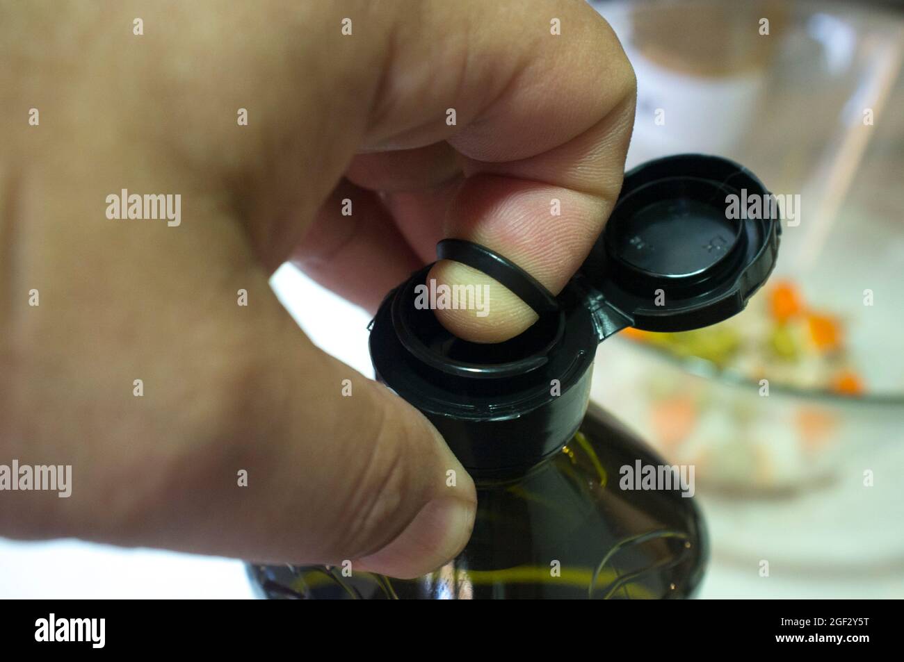 Öffnen einer versiegelten Olivenölflasche mit Finger und einer inneren herausziehbaren Kunststofflasche unter der Kappe. Nahaufnahme Stockfoto