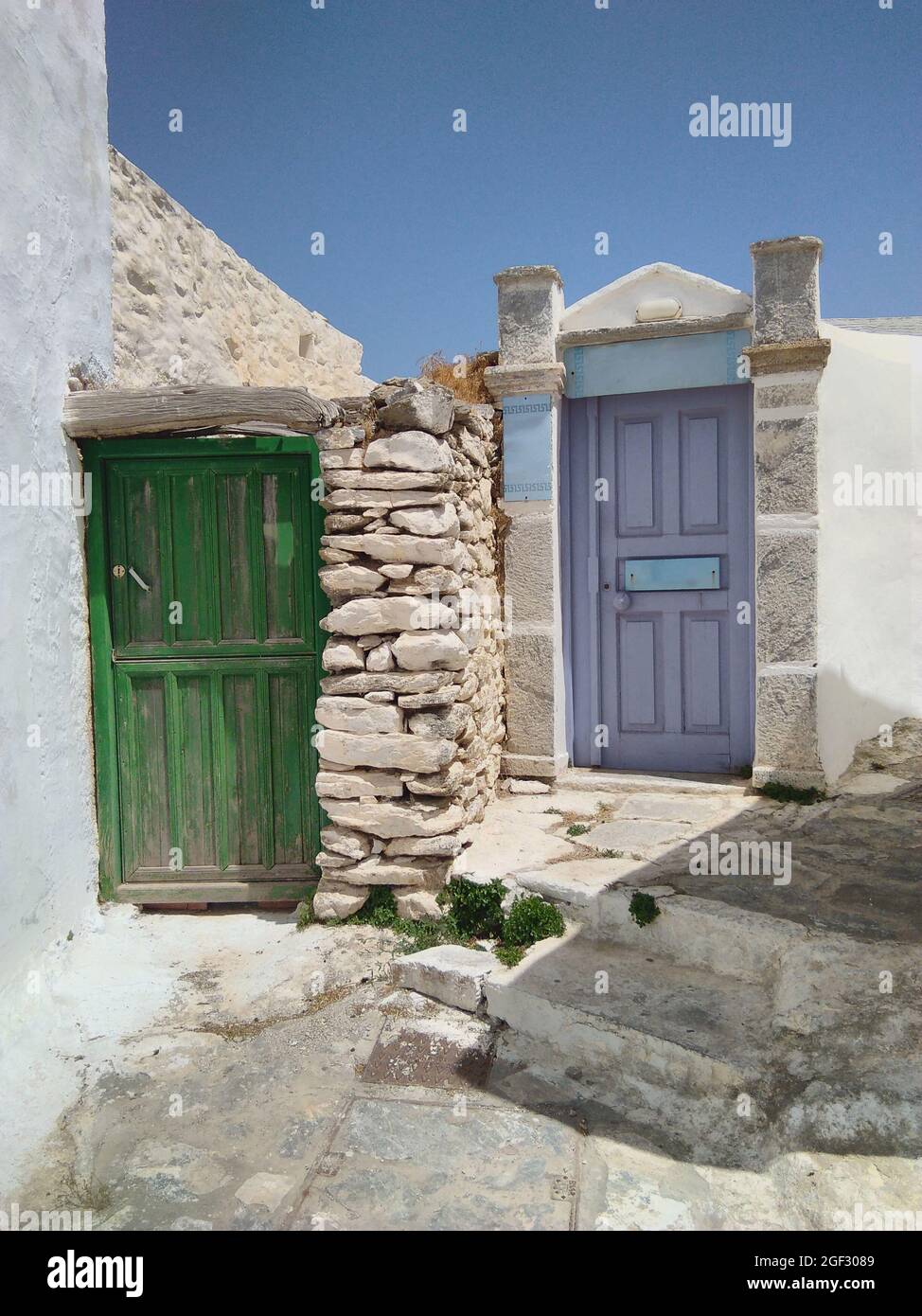 Insel Amorgos, Griechenland. Bunte alte Häuser im traditionellen Dorf. Hell gestrichene Türen in einer Gasse. Vertikale Aufnahme, blauer Himmel und Kopierbereich Stockfoto