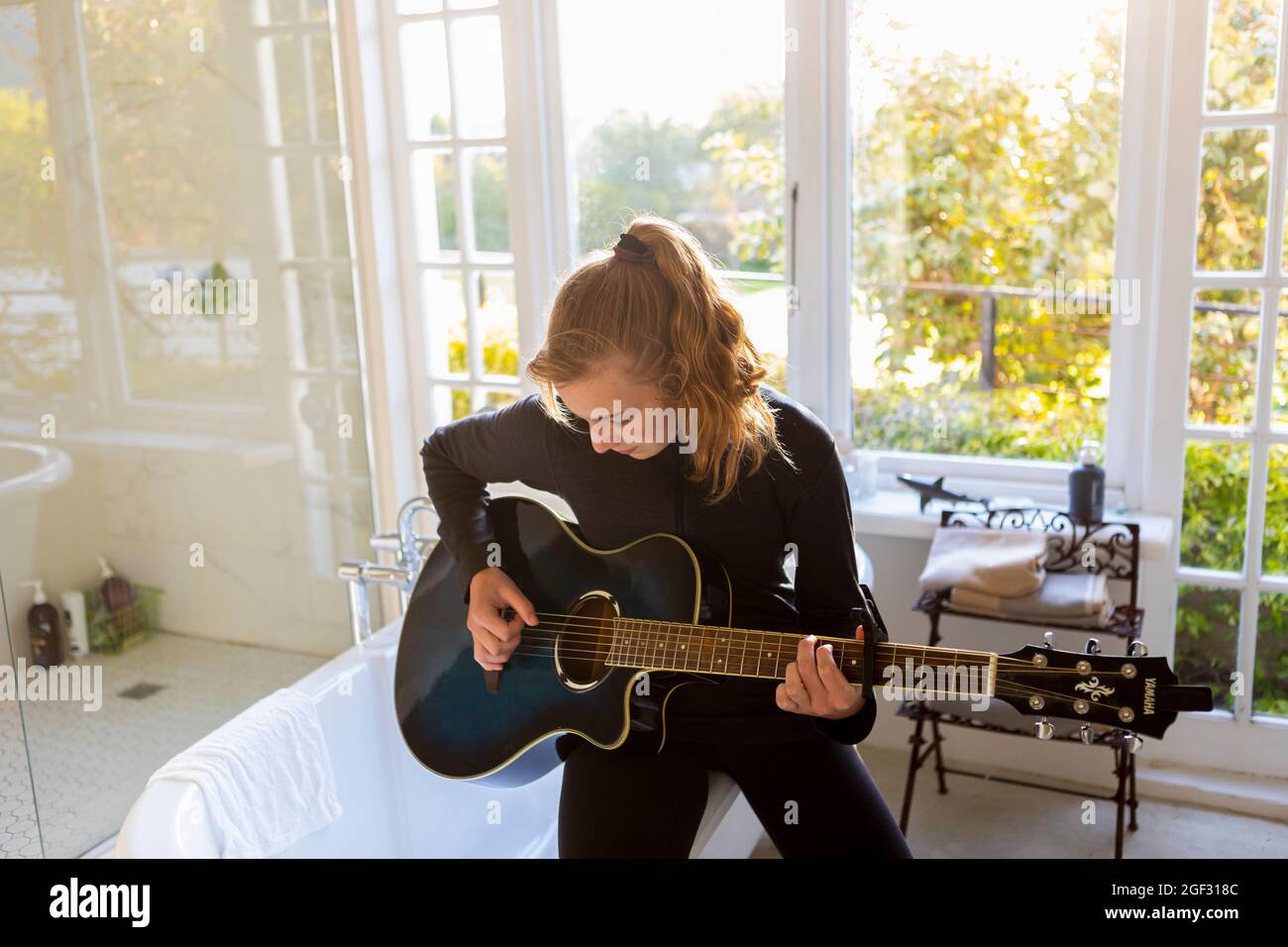 Teenager-Mädchen, das am Rand einer Badewanne saß und akustische Gitarre spielte. Stockfoto
