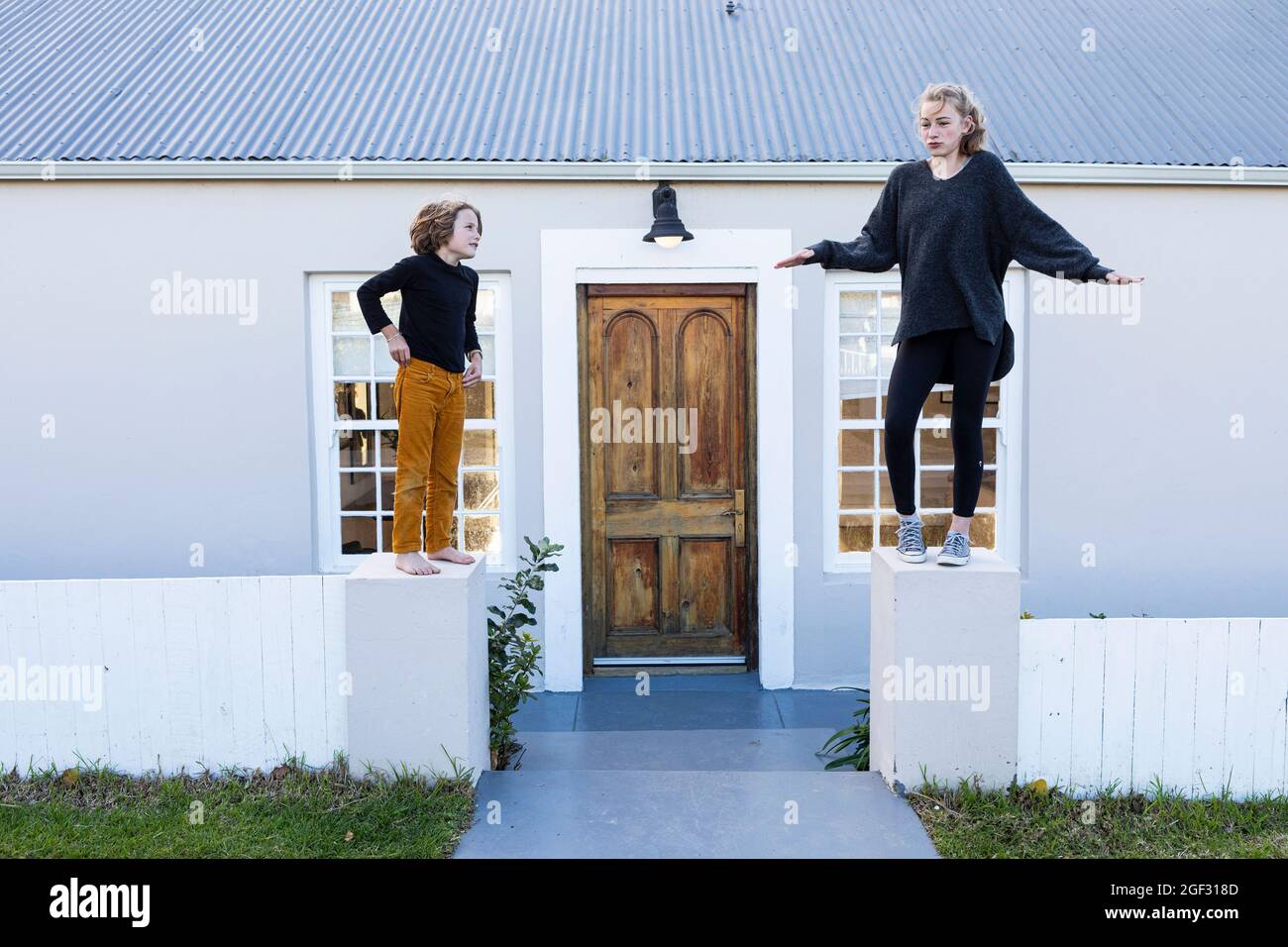 Bruder und Schwester stehen auf einer niedrigen Wand vor einem Haus und lachen Stockfoto