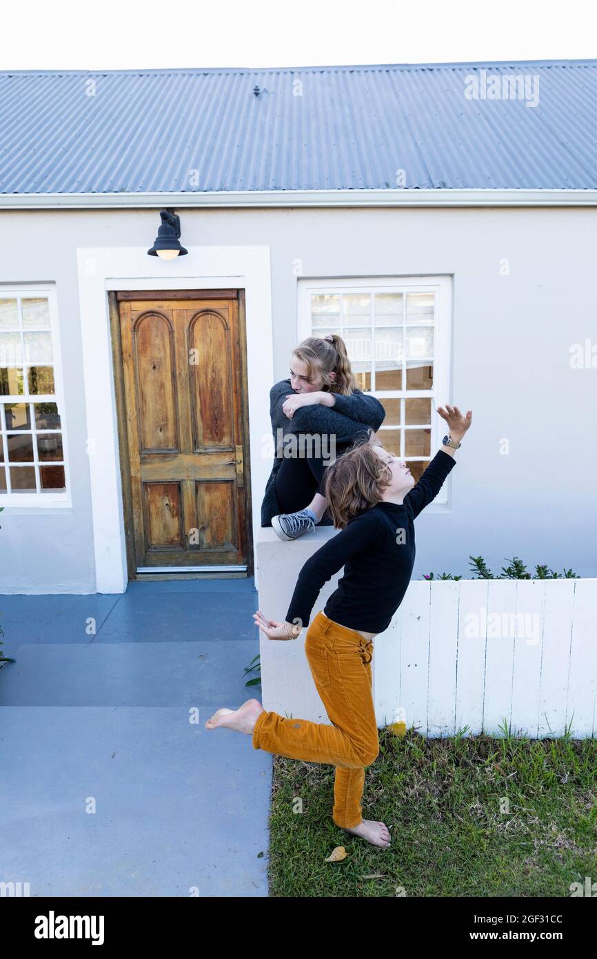 Bruder und Schwester vor ihrem Haus, Junge, der barfuß auf Gras tanzt. Stockfoto