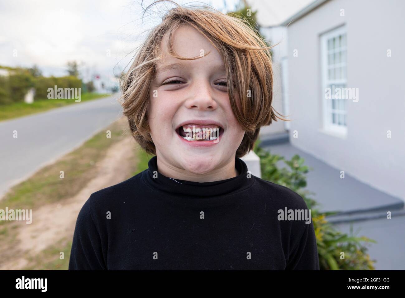 Acht Jahre alter Junge mit einer Nuss zwischen den Zähnen, einem toothy Grinsen Stockfoto