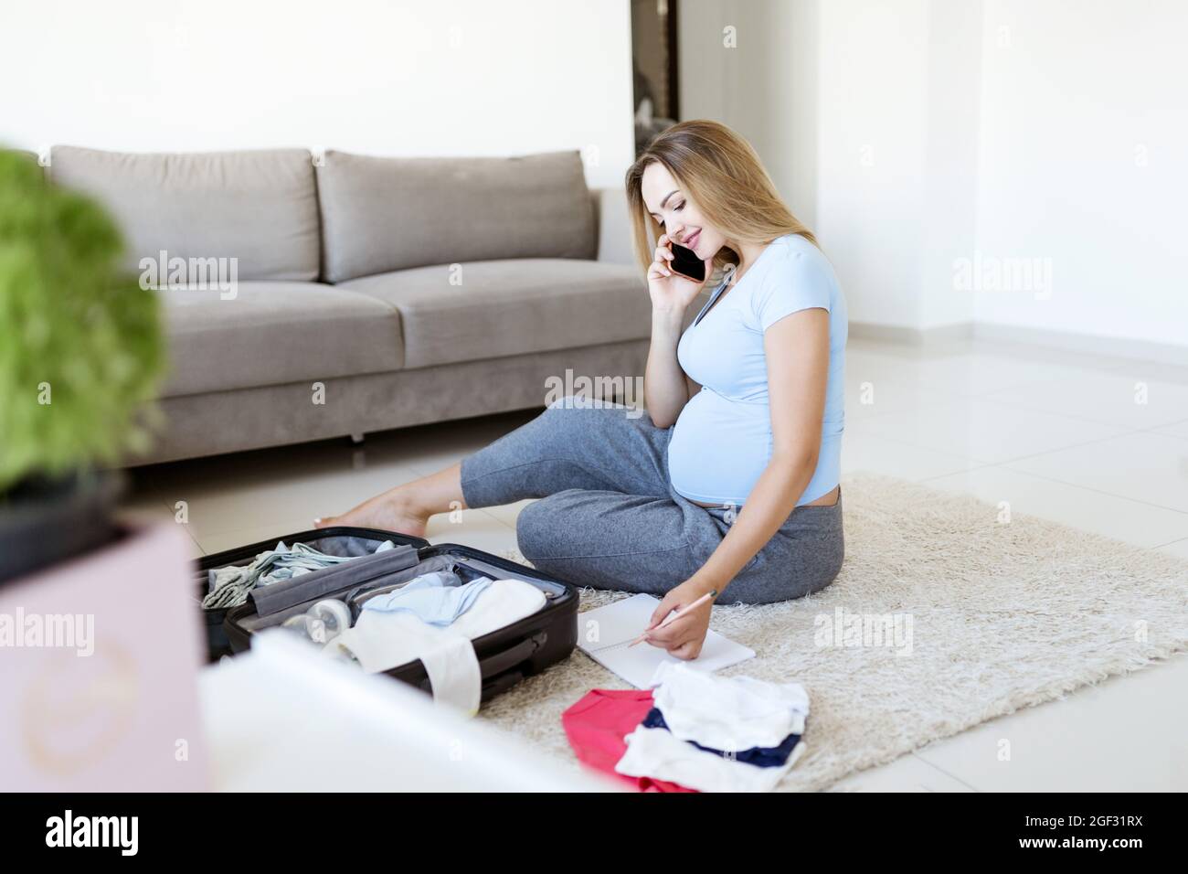 Schwangere in blauem T-Shirt, Checkliste, Telefongespräch und Vorbereitung  Sachen für Entbindungsklinik zu Hause. Glückliche Schwangerschaft  Verpackung Baby Kleidung auf Koffer Stockfotografie - Alamy
