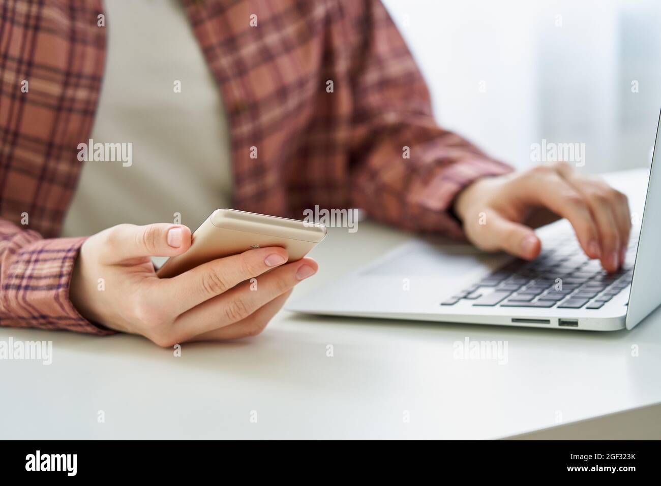 Gesichtslose junge Frau, die beim Tippen auf dem Laptop auf dem Smartphone surft. Millennial-Datenschutzkonzept Stockfoto