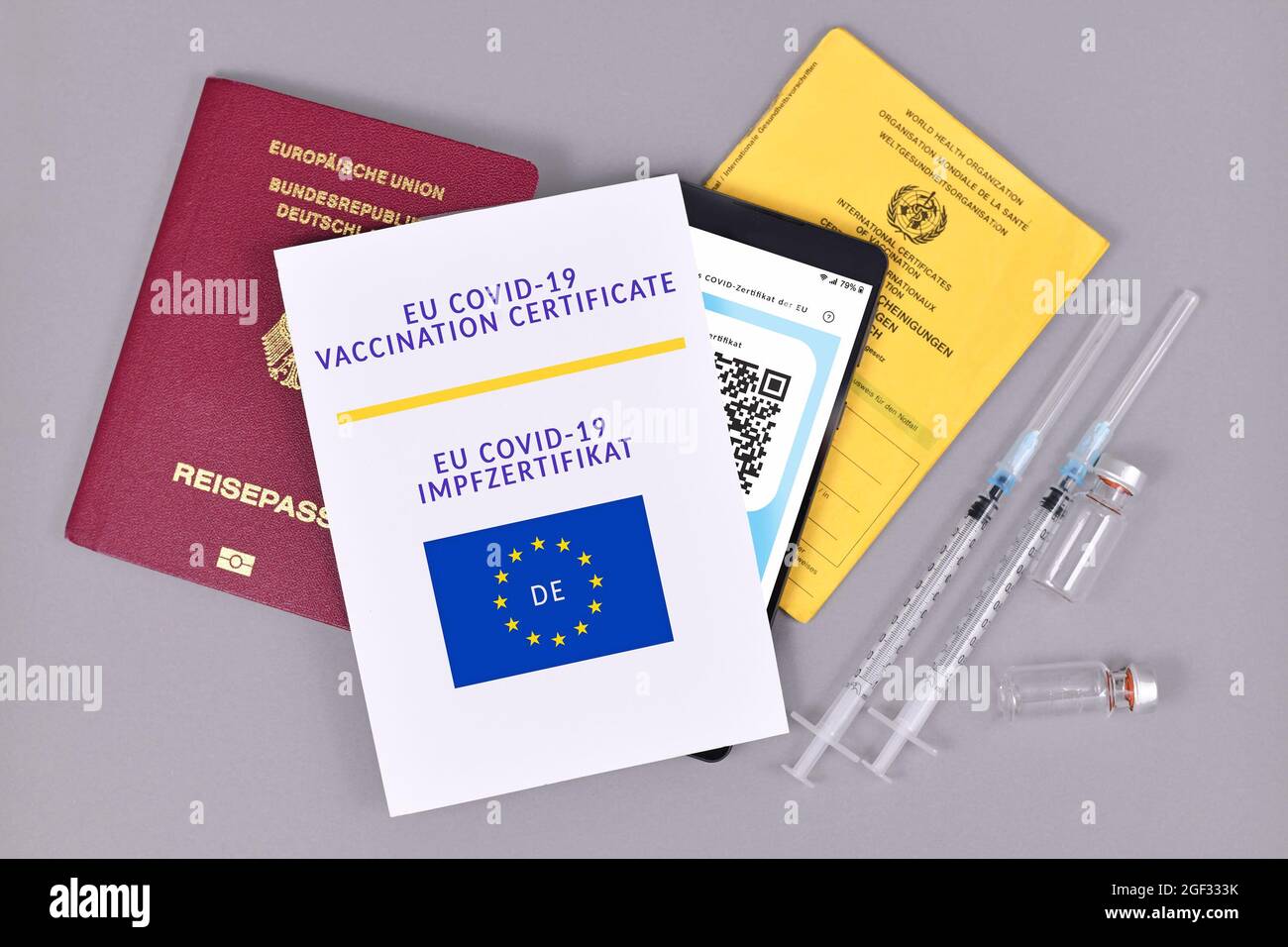 Deutschland - Juli 2021: EU-Impfpass COVID-19 auf Papier und digital am Telefon, Impfpass, Reiseausweis und Spritzen mit Fläschchen auf grauem b Stockfoto
