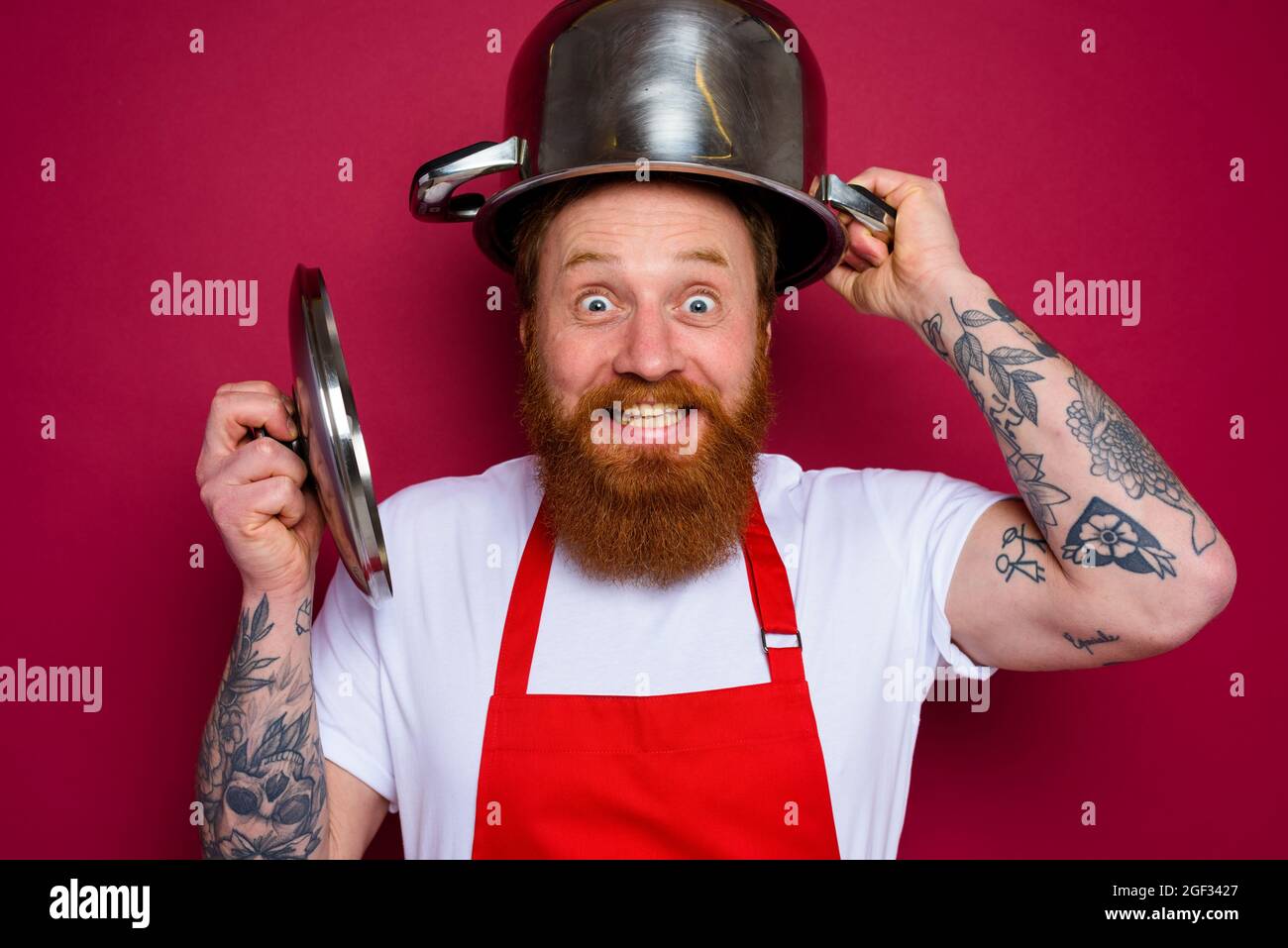 Glücklicher Koch mit Bart und roter Schürze spielt mit Topf Stockfoto