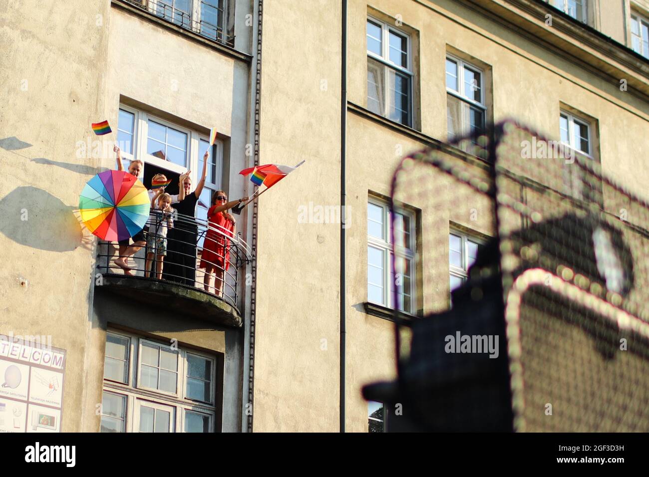 Eine Familie steht auf einem Balkon, während sie mit polnischen und regenbogenfarbenen LGBT-Stolzflaggen zur Unterstützung des marsches winkt. Auch der jährliche Gleichstellungsmarsch ist bekannt Stockfoto