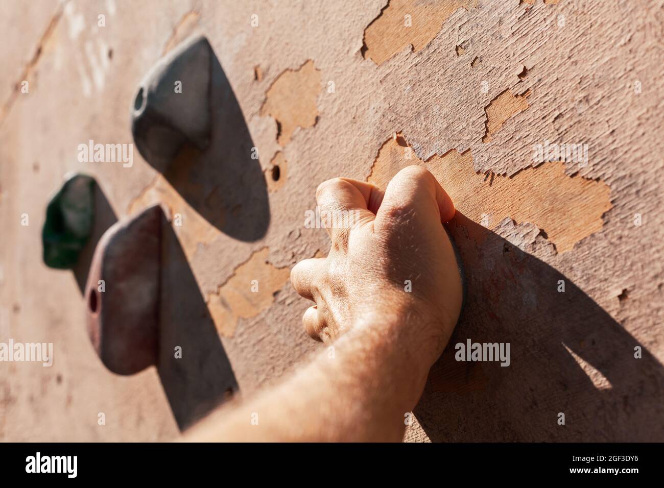 Nahaufnahme der männlichen Hände, die an der abgenutzten Außenwand Klettergriffe greifen. Mann, der Kletterübungen an einer künstlichen Kletterwand im Park macht. Stockfoto