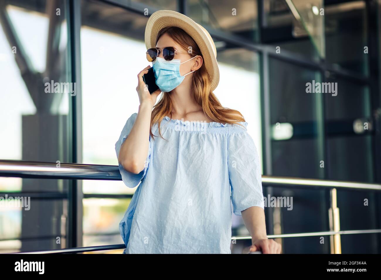 Junge Reisende in einer medizinischen Schutzmaske auf ihrem Gesicht, eine Frau geht mit Koffern und spricht auf einem Handy, am Flughafen, das Konzept der Reise Stockfoto Junge Reisende in einer medizinischen Schutzmaske auf ihrem Gesicht, eine Frau geht mit Koffern und spricht auf einem Handy, am Flughafen, das Konzept der Reise Stockfoto