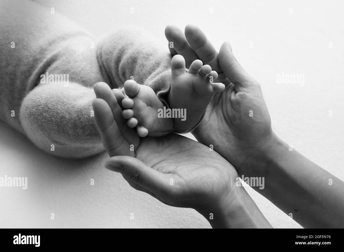 Foto mit Kinderbeinen, die in den Handflächen von Mama und Papa gehalten werden. Schwarz-Weiß-Foto. Familienalbum. Neugeborene Füße. Stockfoto