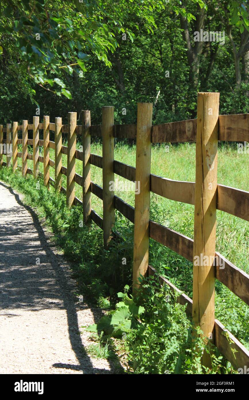Traditioneller hölzerner Grenzzaun, der an einem hellen sonnigen Sommertag ein Farmfeld überquert. Stockfoto