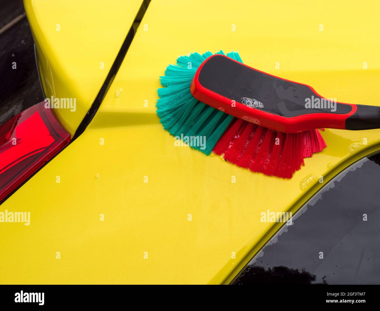 Nahaufnahme einer weichen Borstenbürste und Seifenwasser, das zum Reinigen/Waschen der Lackierung eines gelben Autos verwendet wird. Stockfoto