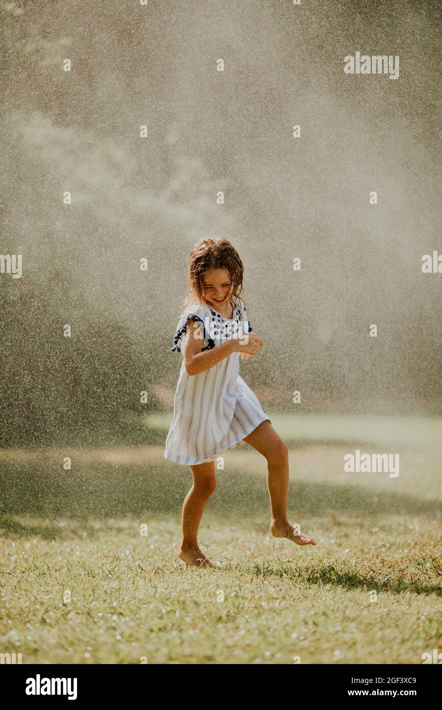 Nettes kleines Mädchen, das Spaß mit Wasser unter Bewässerungsregner hat Stockfoto