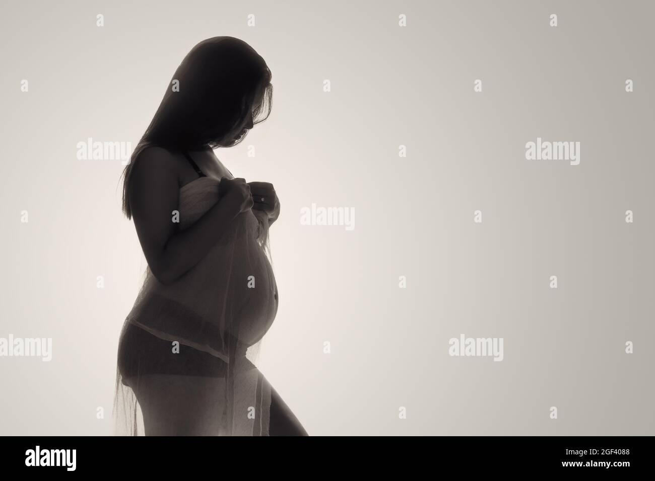Hintergrundbeleuchtetes Low-Key-Foto einer jungen Schwangeren. Stockfoto