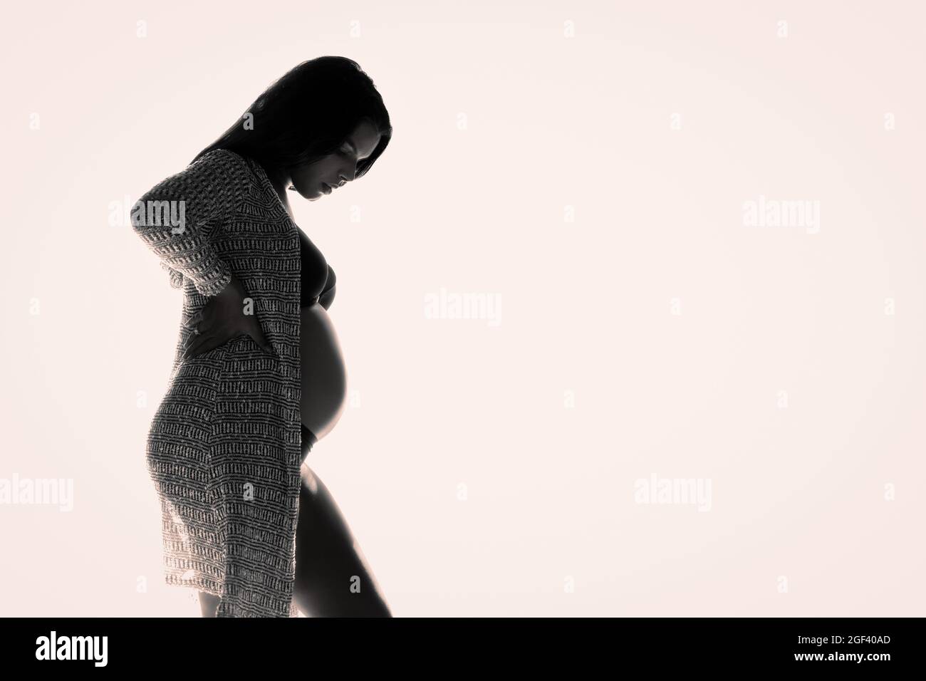 Hintergrundbeleuchtetes Low-Key-Foto einer jungen Schwangeren. Stockfoto