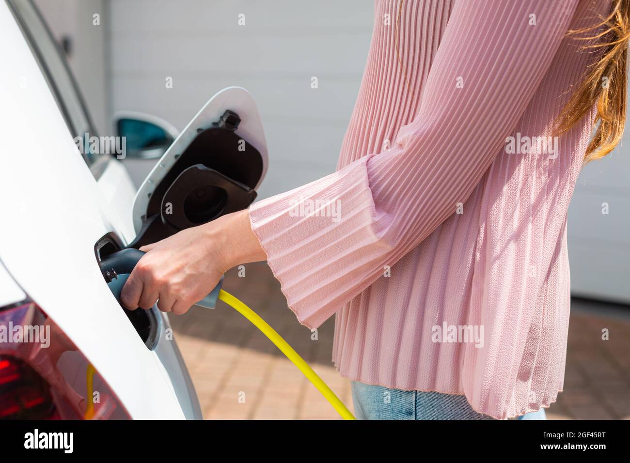 Nahaufnahme einer kaukasischen weiblichen Hand, die ein Elektroauto mit eingestecktem Netzkabel lädt Stockfoto