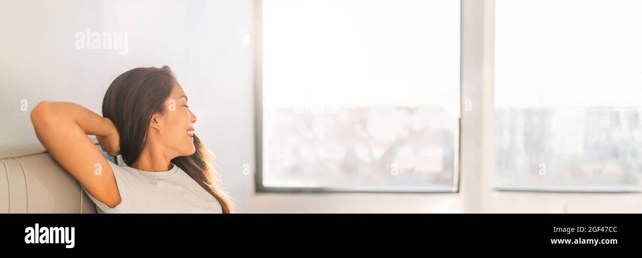 Saubere Raumluft glückliche asiatische Frau atmet zu Hause aus Luftreiniger sitzen auf dem Sofa Blick aus dem Fenster Panorama-Banner Stockfoto