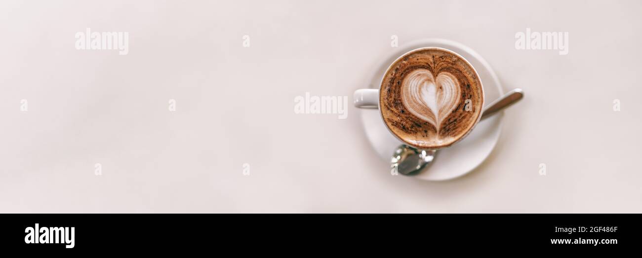 Latte Art Kaffeebecher von oben am Kaffeetisch mit weißem Hintergrund und Panoramafanner mit herzförmigem Schaumstoff von Barista Stockfoto