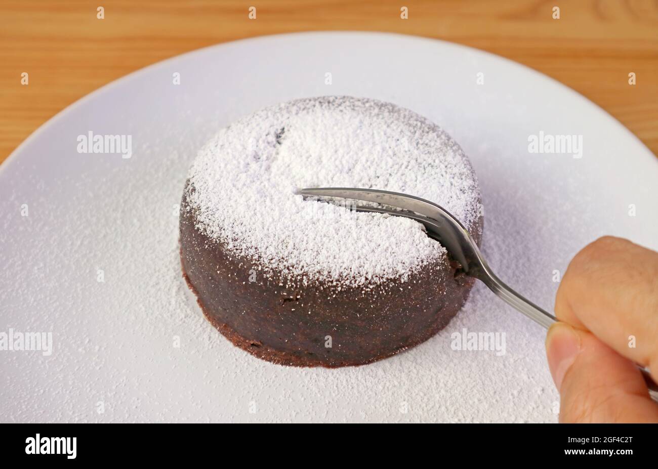 Gabelschnitt in einen köstlichen reichen Schokoladenkuchen, der mit Puderzucker bestreut ist Stockfoto