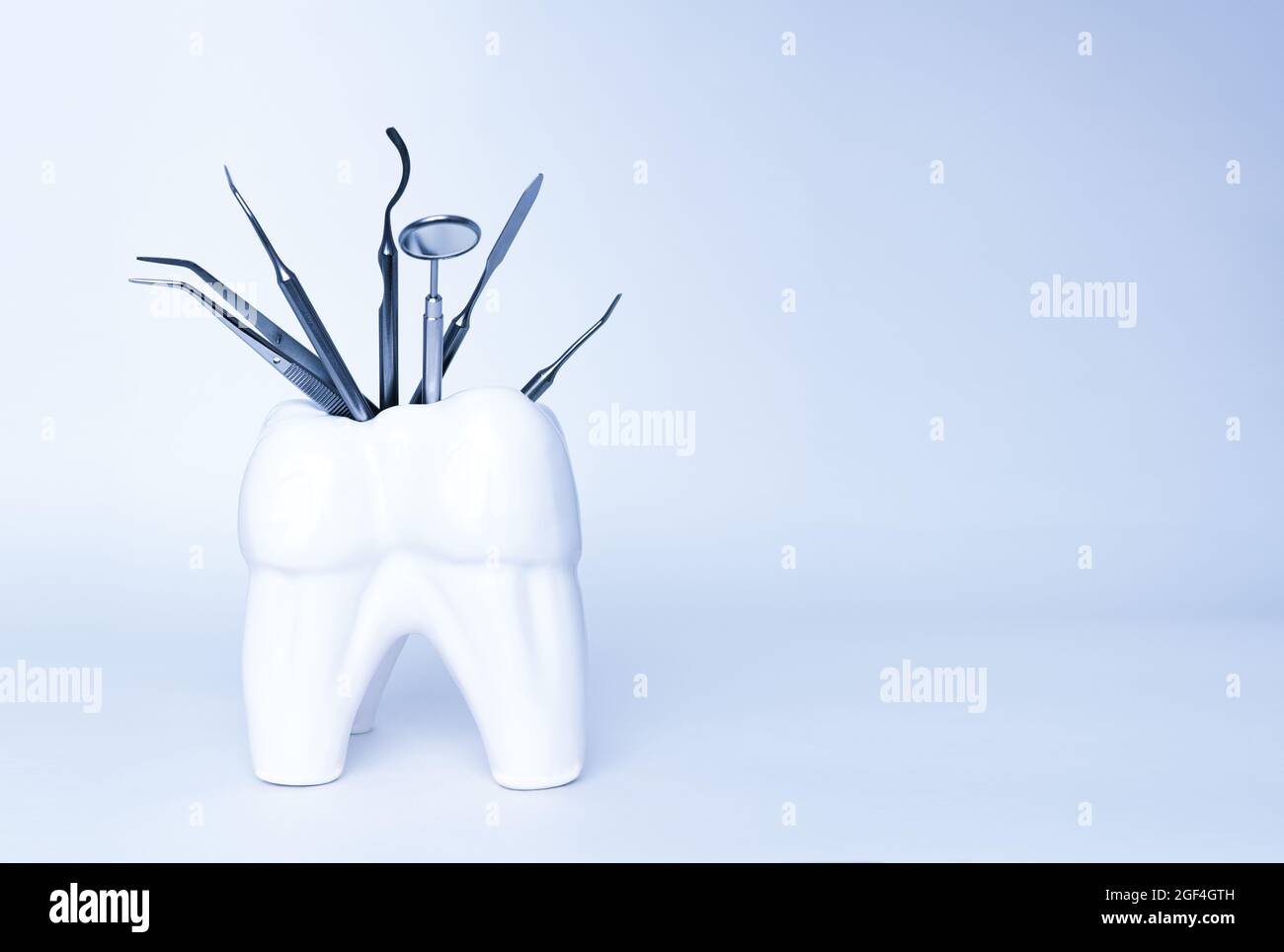 Zahnärztliche Profi-Stahlwerkzeuge in zahnförmigem Halter auf blauem Hintergrund. Set von medizinischen Geräten aus Metall für die Zahnpflege. Sichelsonde Stockfoto