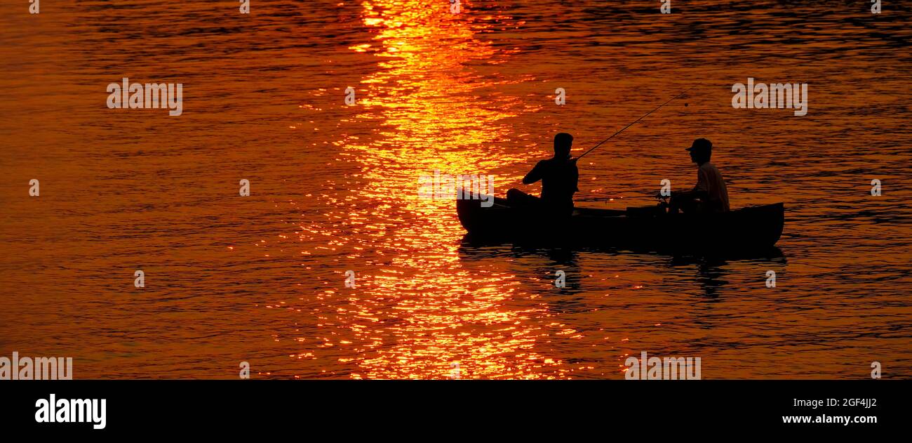 Zwei 2 Personen, die bei Sonnenuntergang bei Sonnenaufgang im See oder im Fluss angeln Stockfoto