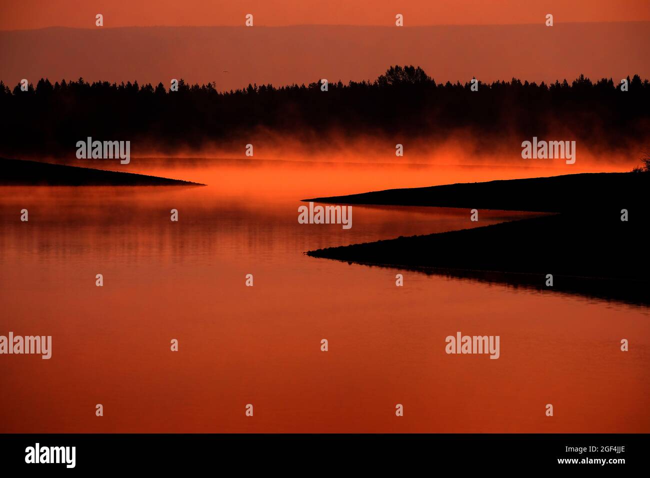 Nebliger Morgen auf dem See mit Dampf, der aus dem Sonnenlicht des Wassers aufsteigt Stockfoto
