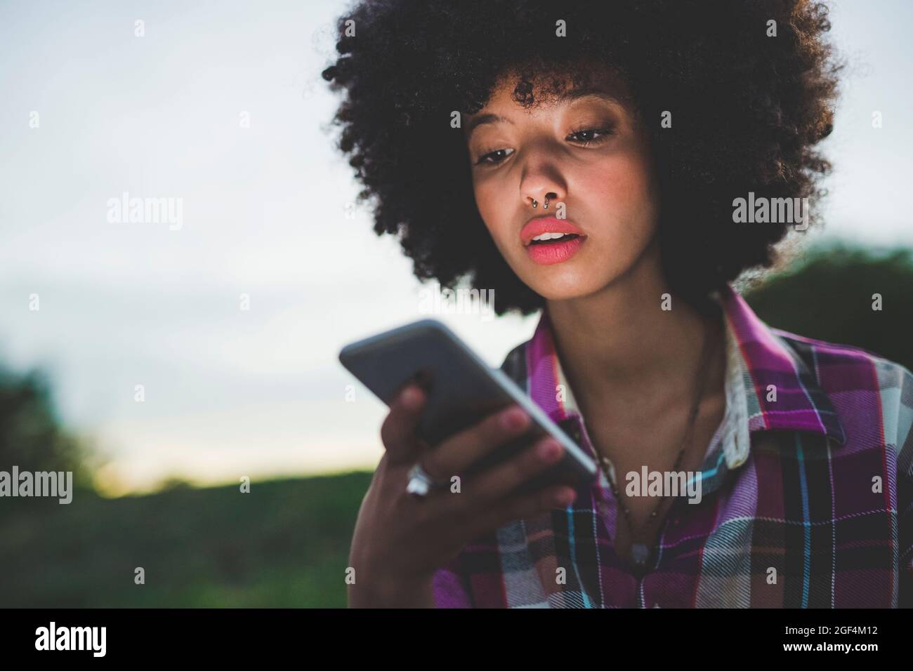 Porträt einer jungen Frau mit Afro-Frisur mit Smartphone im Freien in der Dämmerung Stockfoto