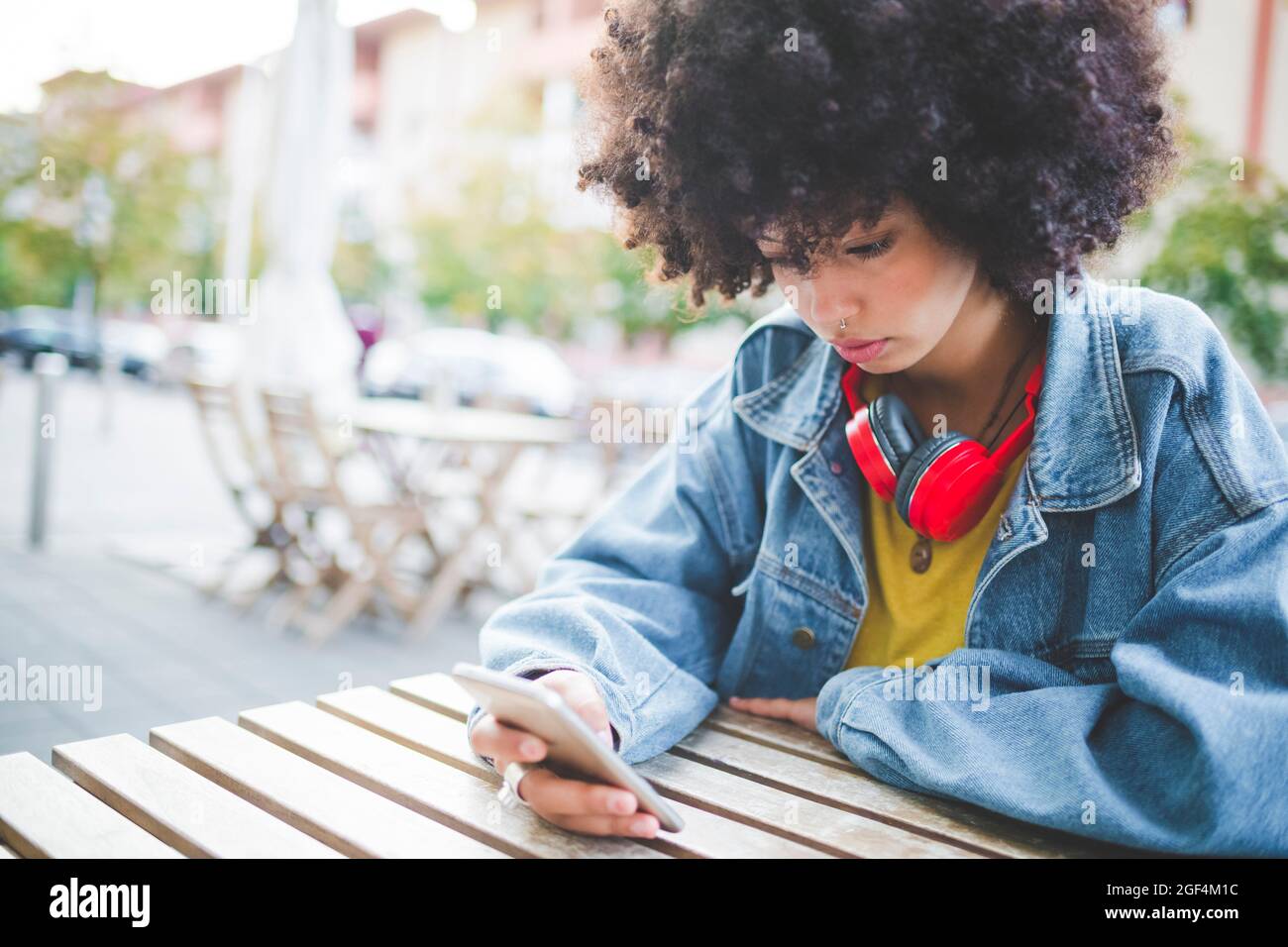 Junge Frau mit Afro-Frisur mit Smartphone in einem Café im Freien in der Stadt Stockfoto