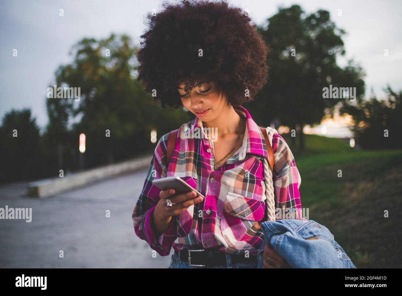 Junge Frau mit Afro-Frisur mit Smartphone im Freien in der Dämmerung Stockfoto