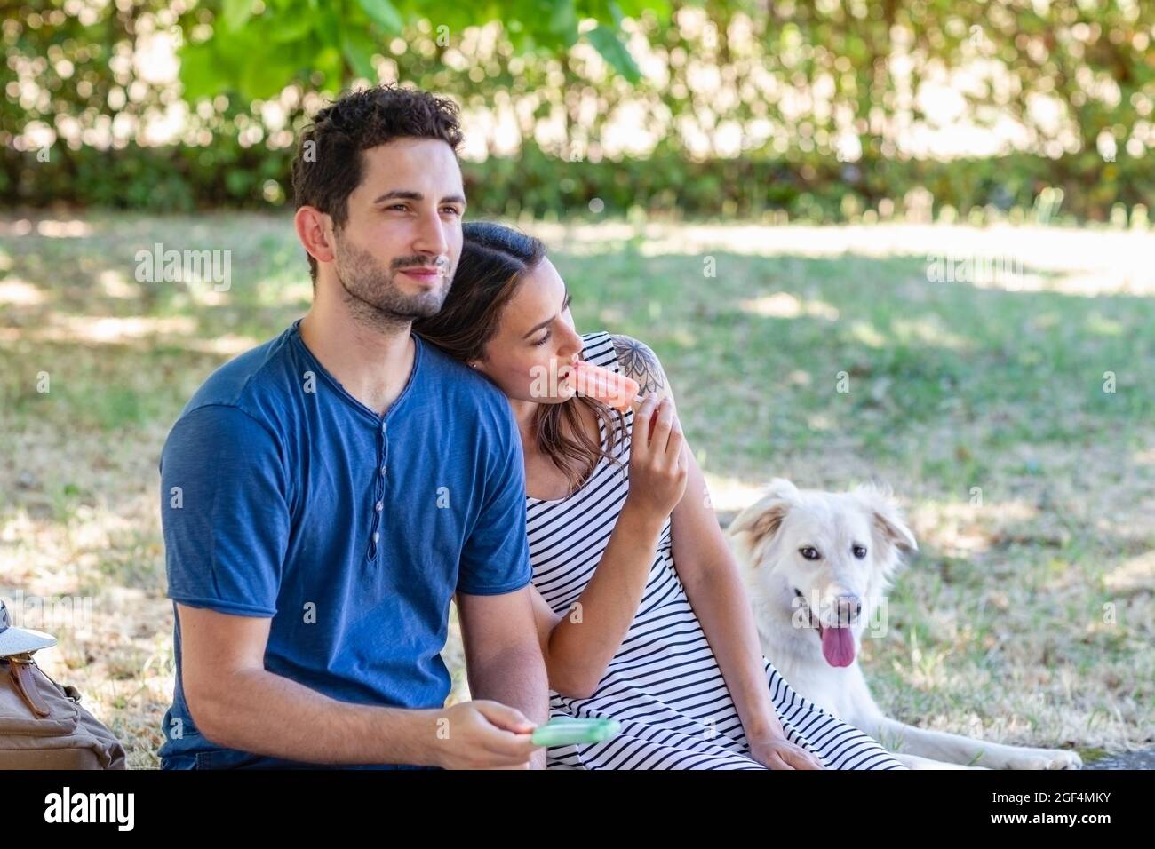 Freundin isst Eis, während sie sich vom Hund auf die Schulter des Freundes lehnt Stockfoto