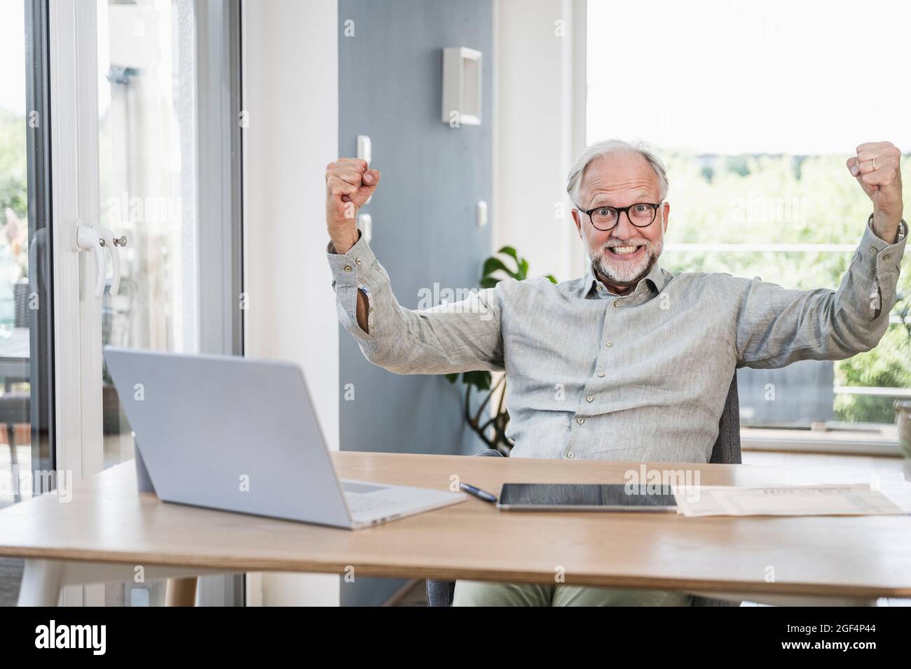 Fröhlicher Geschäftsmann, der sich die Faust zuklammernden, während er im Home Office am Schreibtisch sitzt Stockfoto