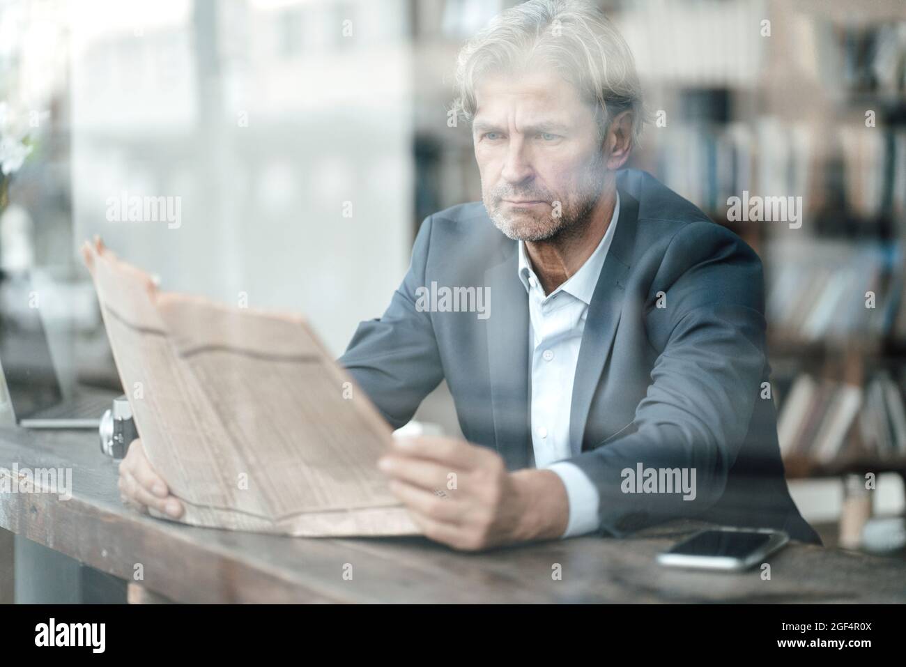 Reifer Geschäftsmann liest Zeitung, sitzt im Café durch das Glasfenster gesehen Stockfoto