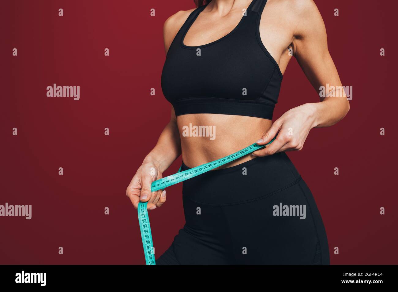 Sportlerin für mittlere Erwachsene, die die Taille misst, mit Klebeband vor kastanienbraunem Hintergrund Stockfoto