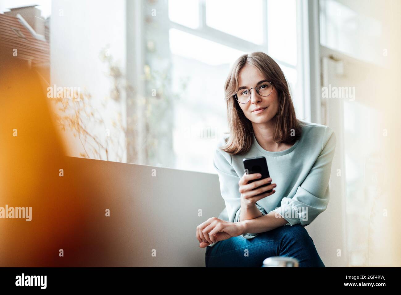 Junge Frau, die mit dem Mobiltelefon im Café sitzt Stockfoto