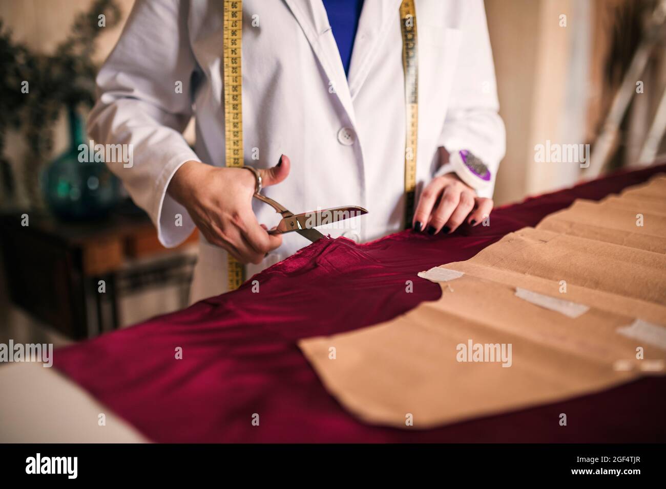 Weibliche Schneiderin schneidet kastanienbraunen Seidenstoff mit Schere in der Werkstatt Stockfoto