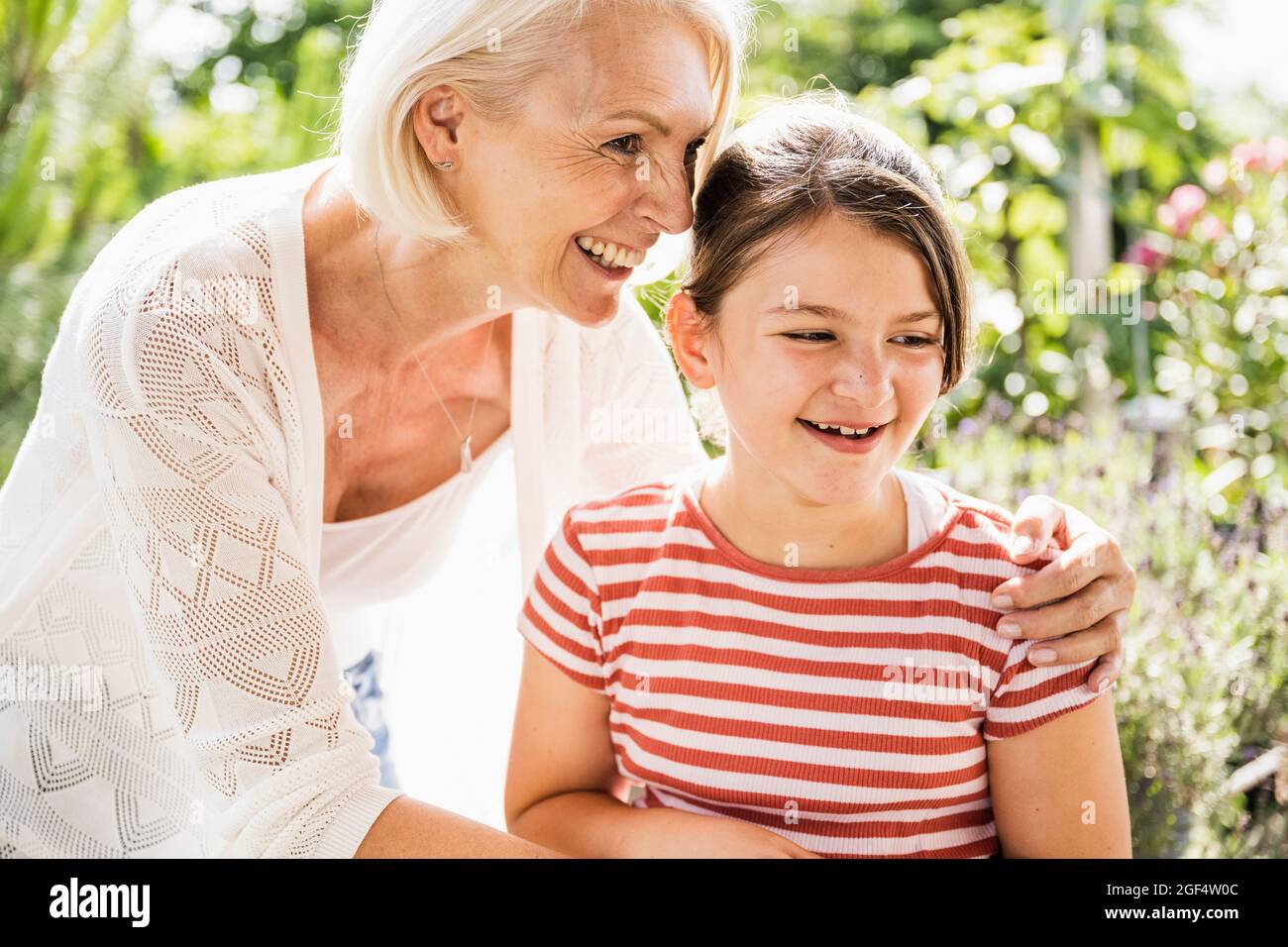 Lächelnde Großmutter, die mit dem Arm um die Enkelin steht Stockfoto