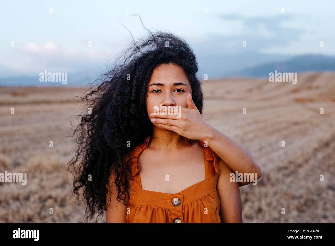 Junge Frau, die den Mund einer Freundin mit der Hand auf dem Bauernhof bedeckt Stockfoto