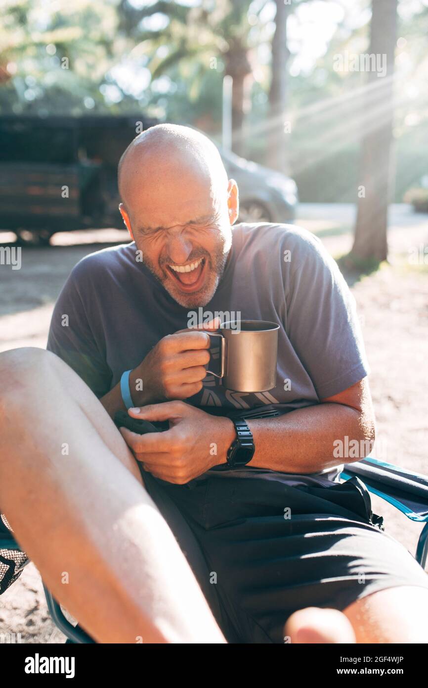 Unbeschwerter Mann mit Kaffeebecher lacht an sonnigen Tagen im Urlaub Stockfoto