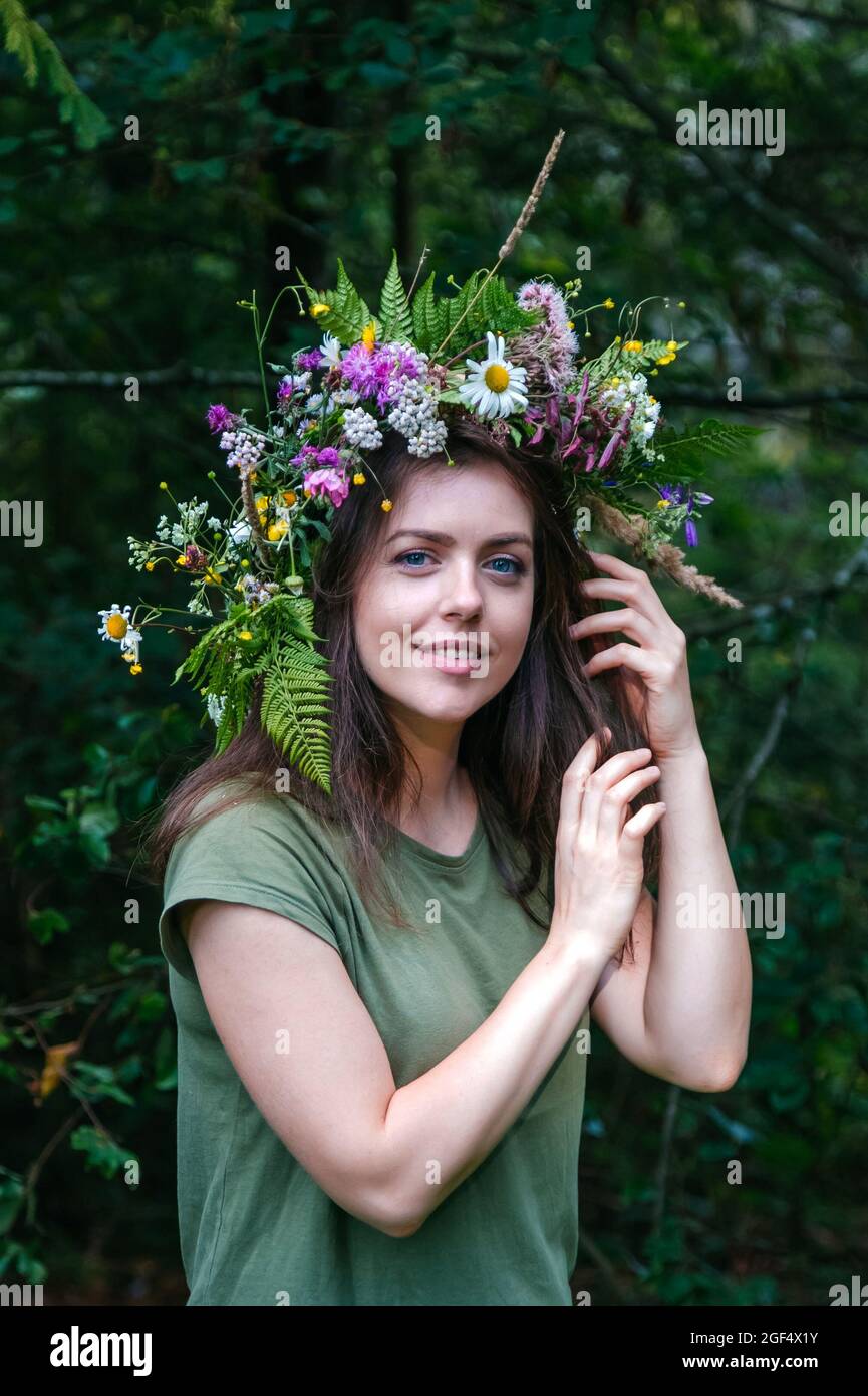 Portrait junge schöne Frau im Kranz von Wildblumen mit Farn im Wald. Blumenkräuterkranz auf dem Kopf der kaukasischen jungen Frau mit langem Braun Stockfoto