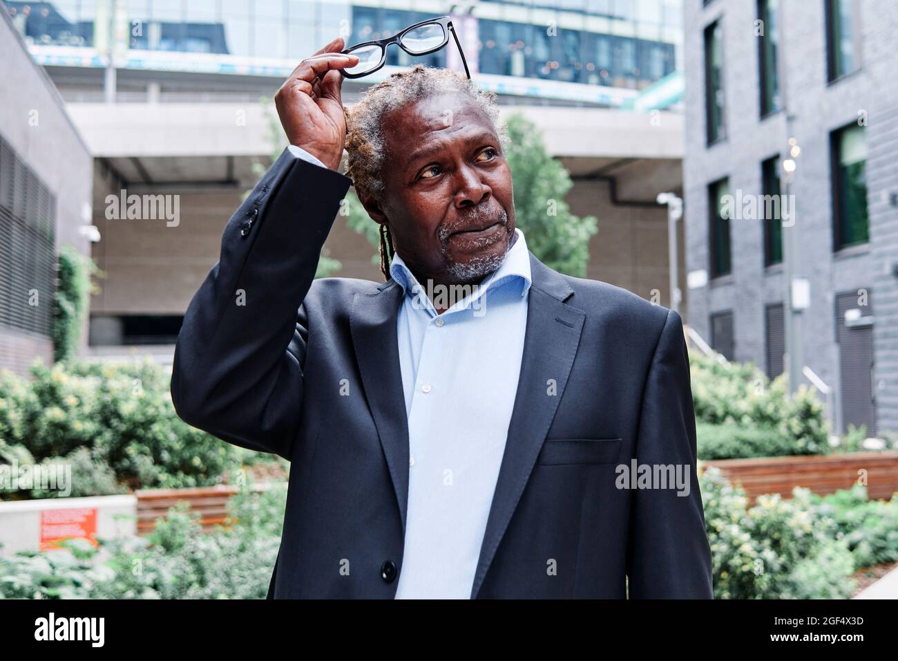 Älterer männlicher Profi, der im Garten stehend Brillen entfernt Stockfoto