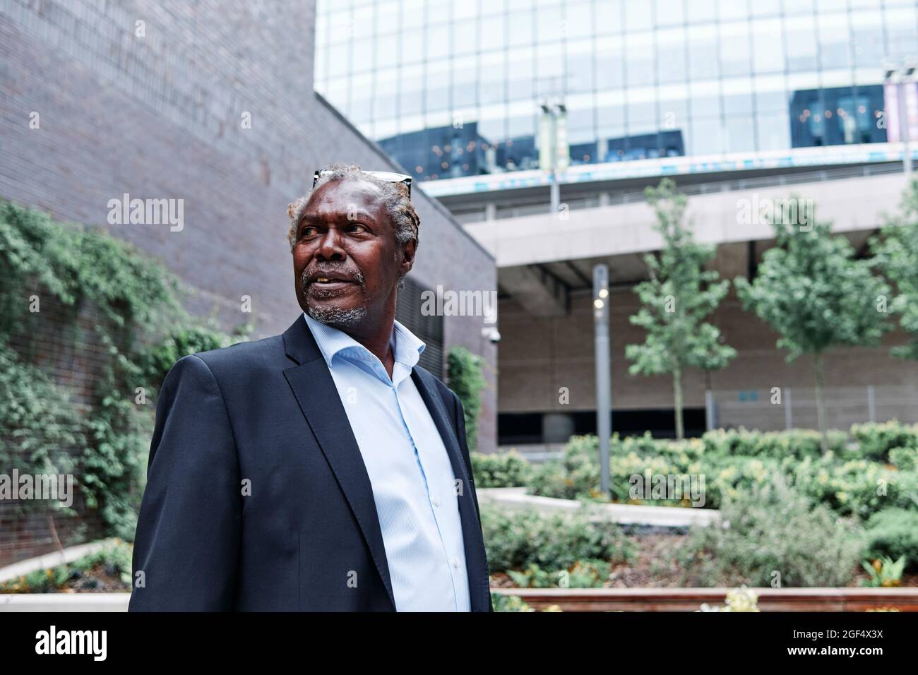 Nachdenklicher älterer männlicher Profi mit Brillen, die im formellen Garten stehen Stockfoto
