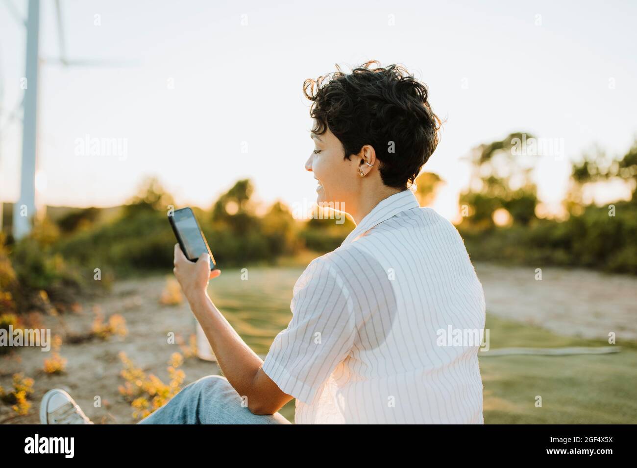 Frau mit kurzen Haaren mit Smartphone bei Sonnenuntergang Stockfoto