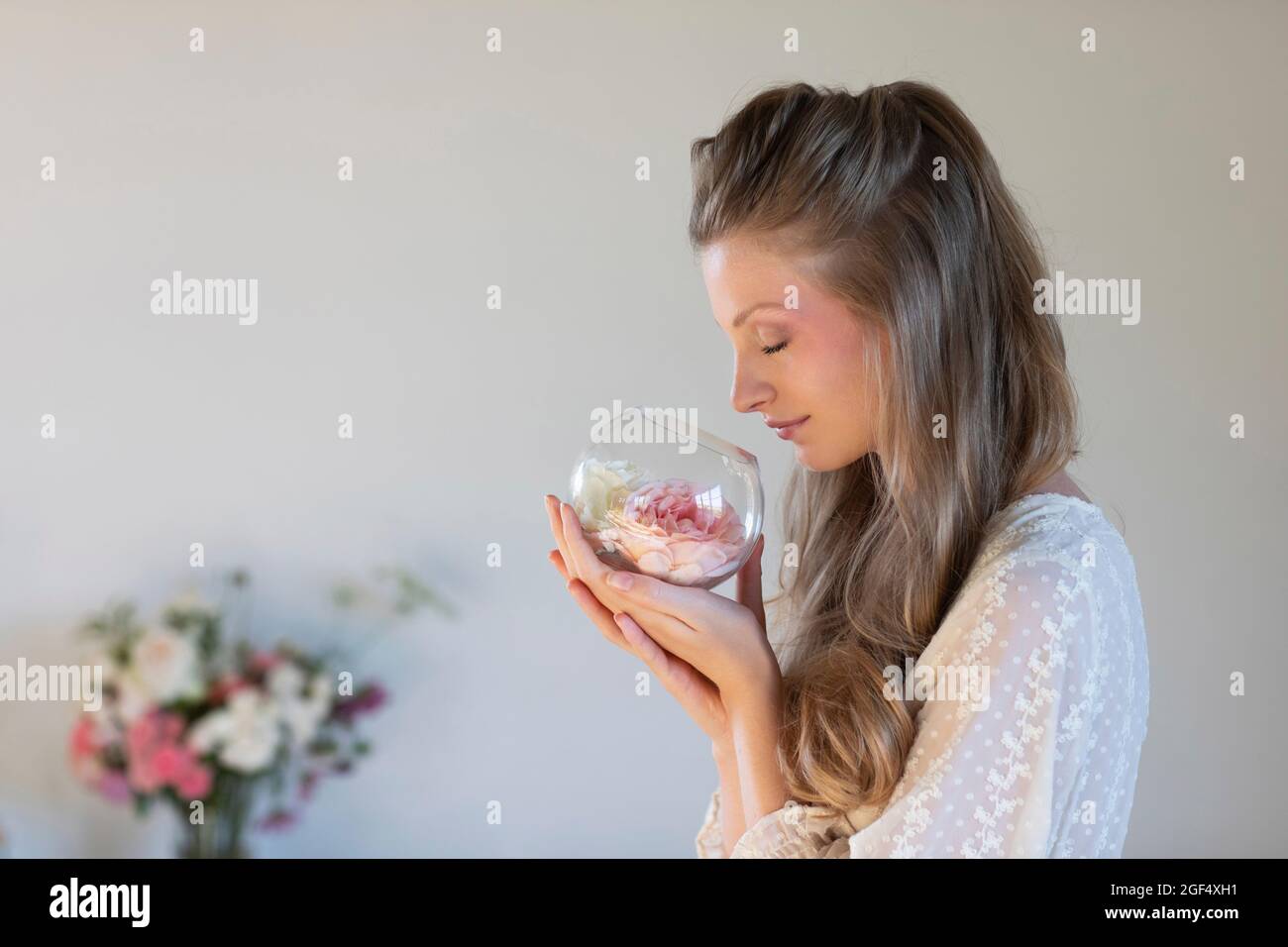Schöne junge Frau riecht duftende Rosen in Terrarienschale Stockfoto