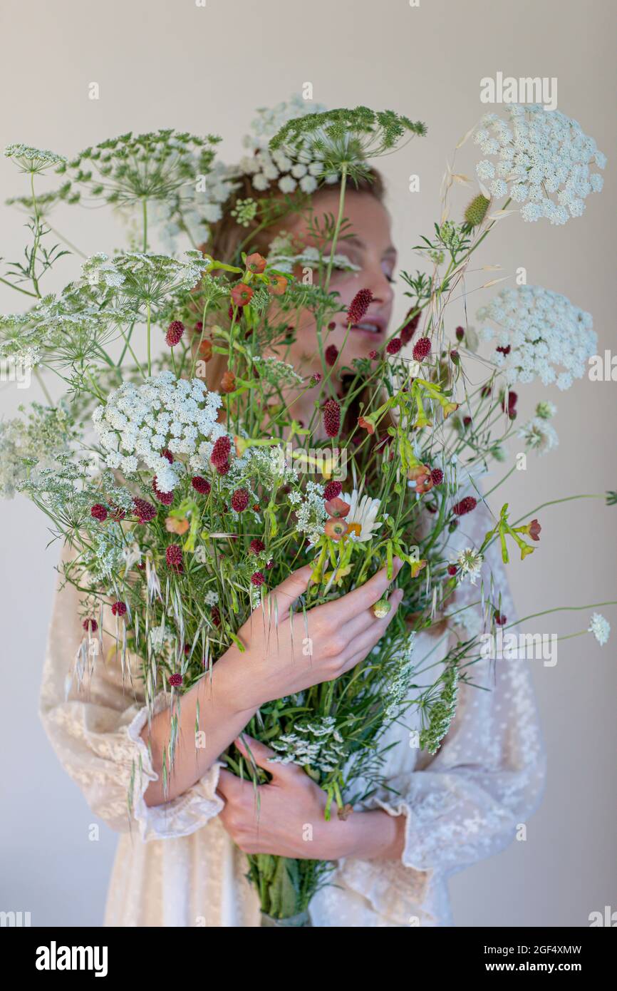 Junge Frau bedeckt Gesicht mit wilden Blumen vor weißem Hintergrund Stockfoto