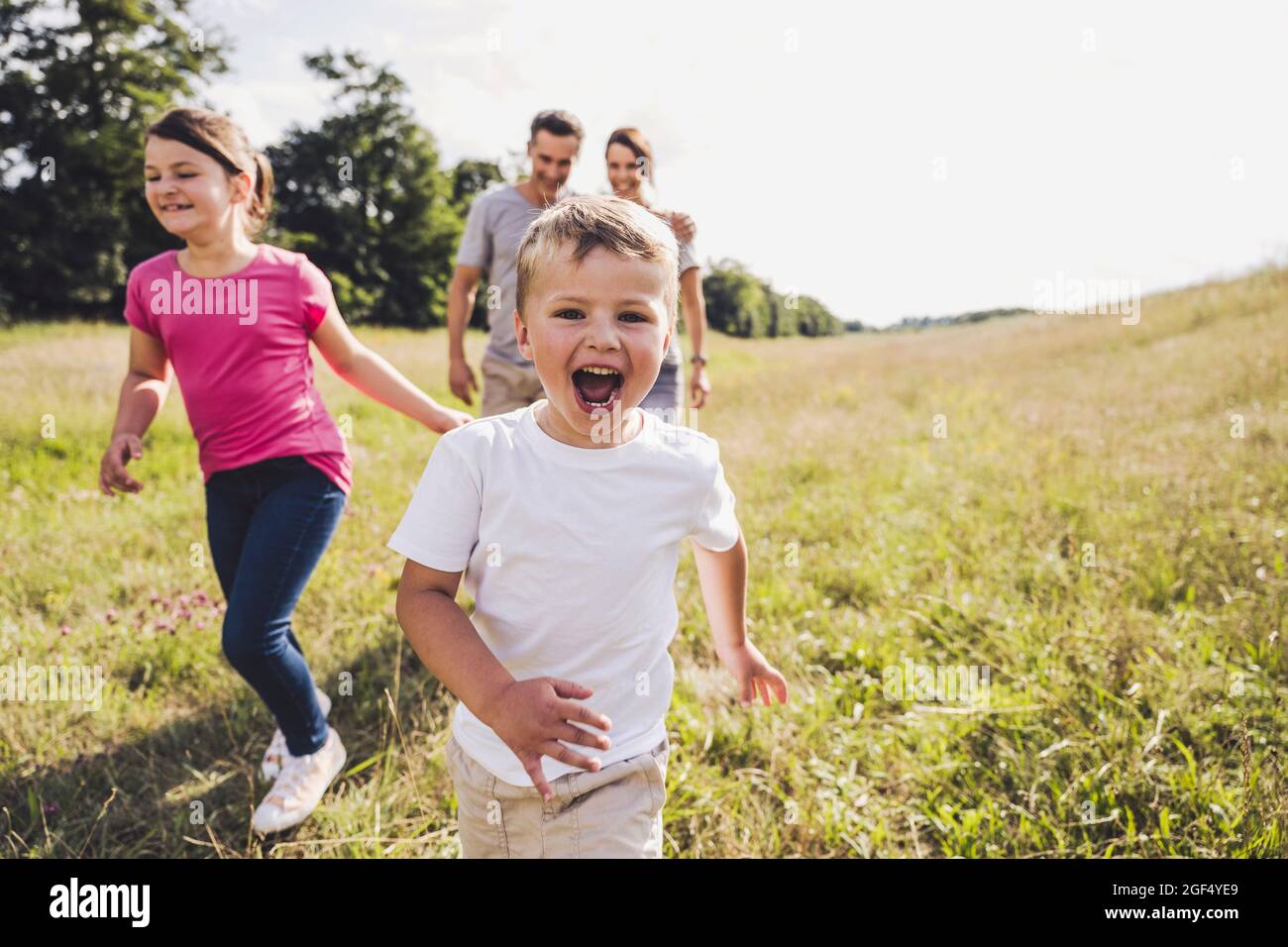 Fröhlicher Junge mit offenem Mund, der an einem sonnigen Tag vor der Familie läuft Stockfoto