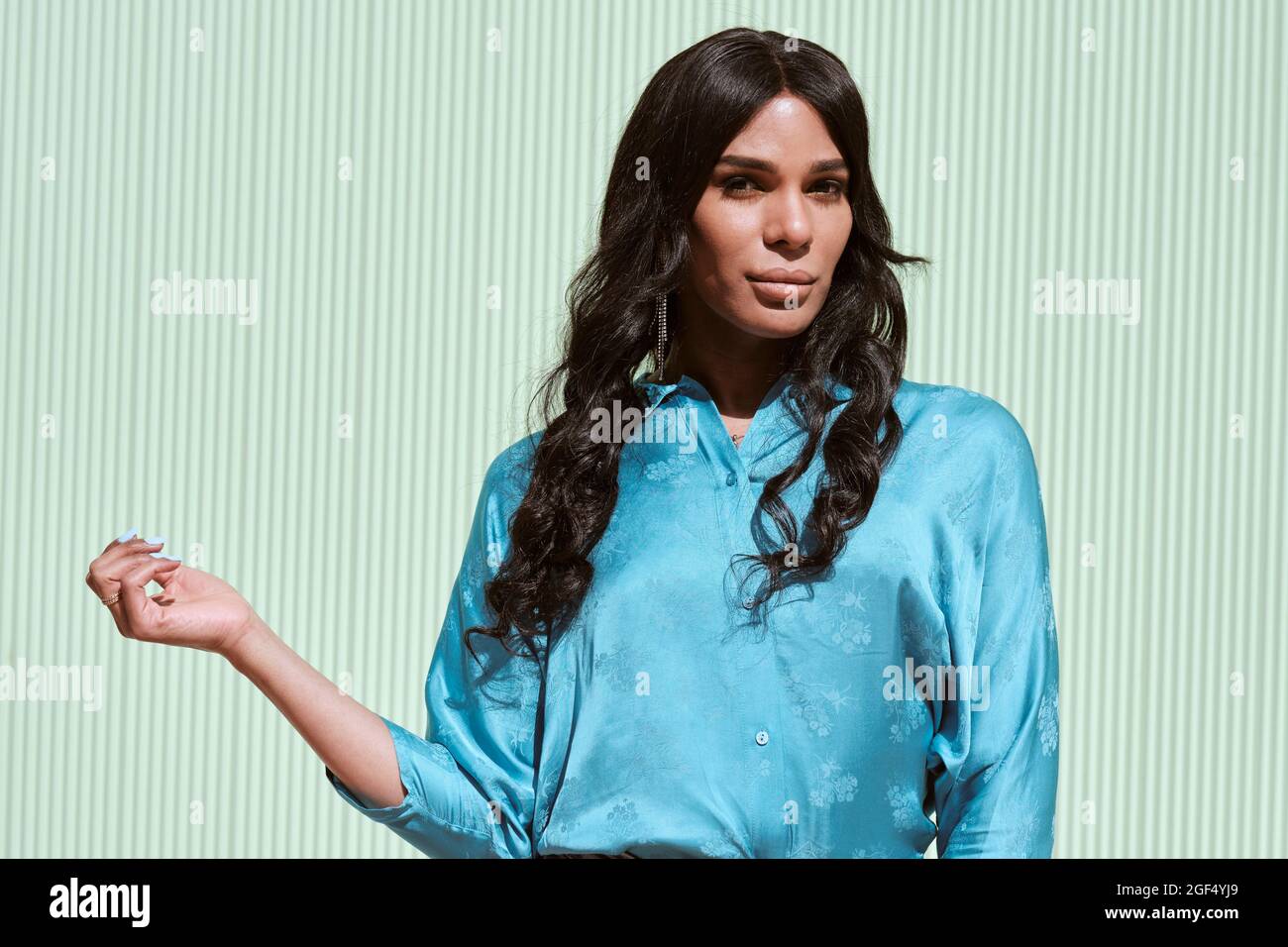 Modische weibliche Transgender, die vor einer hellblauen Wand steht Stockfoto